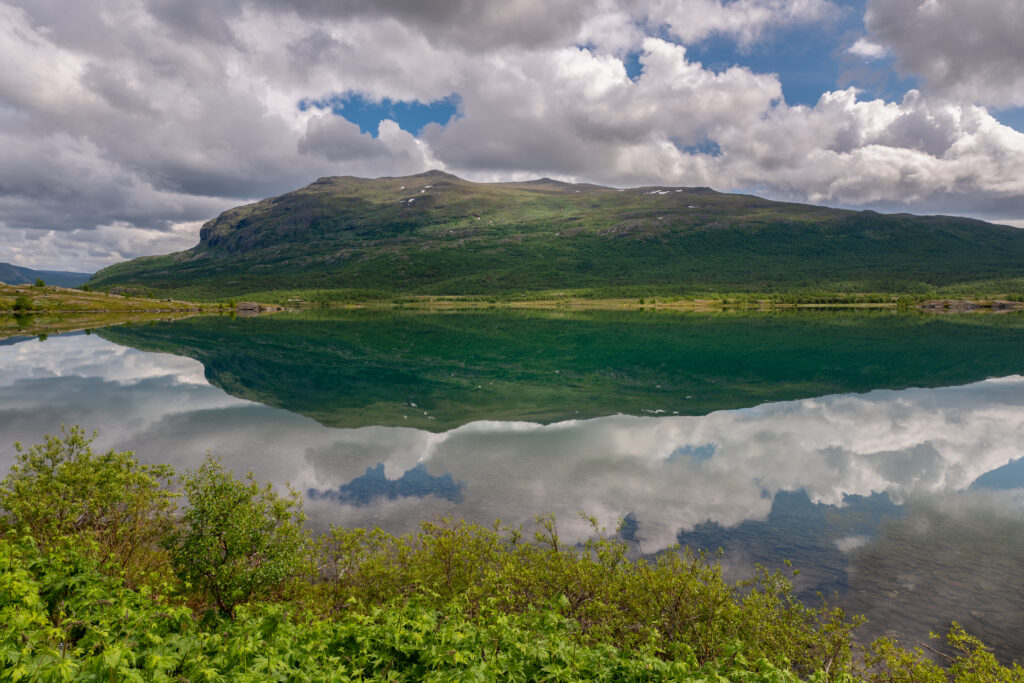 Serene mountain landscape with lush green slopes reflected in calm lake under blue sky clouds Wallpaper