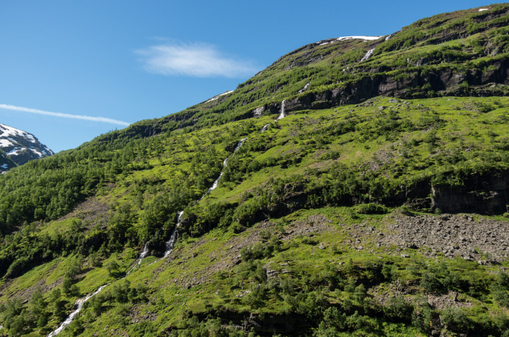 Lush green mountain slopes with a clear blue sky and a cascading stream in nature wallpaper