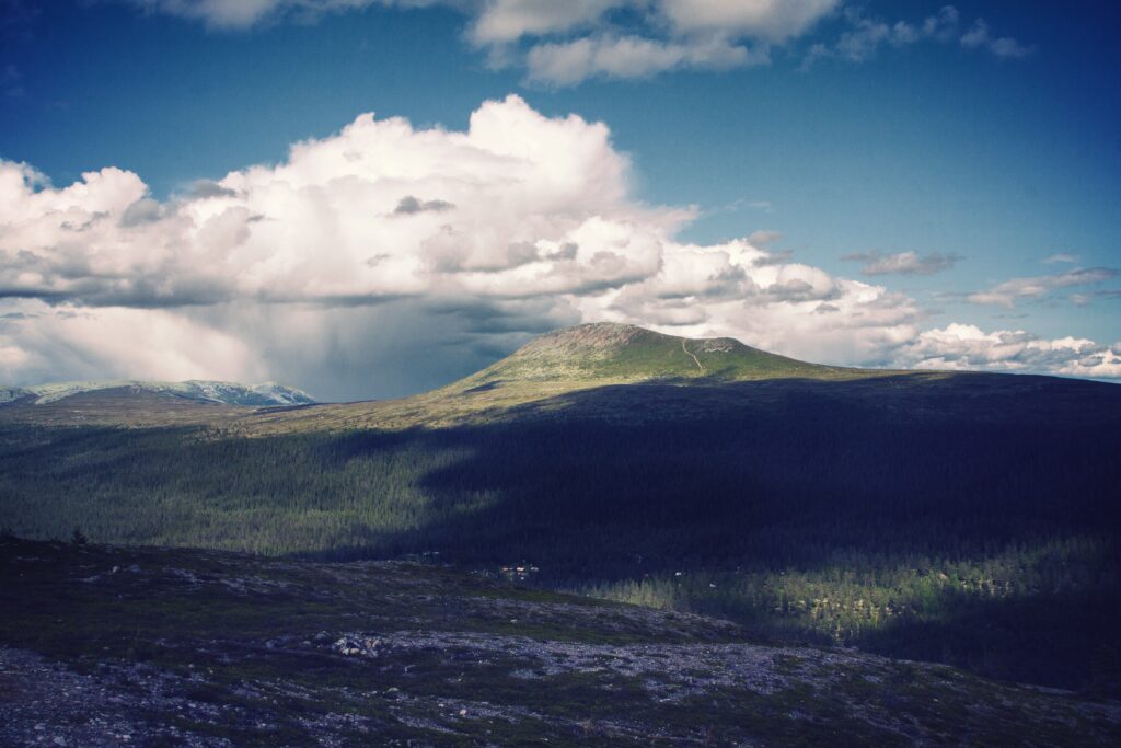 Serene mountain landscape with lush green forest rolling hills and dramatic cloudy blue sky wallpaper