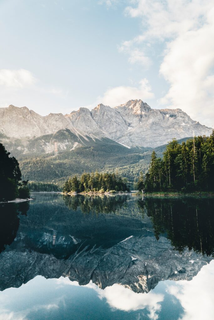 Serene mountain landscape with rugged peaks reflected in calm lake surrounded by forests wallpaper