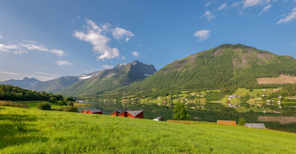 Serene landscape wallpaper with green grass river village and towering mountain peaks under blue sky