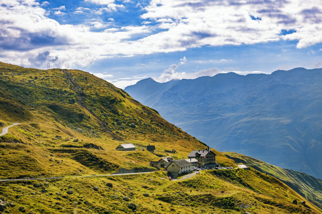 Vibrant wallpaper of rolling hills steep mountains rustic houses green grass and cloudy sky landscape