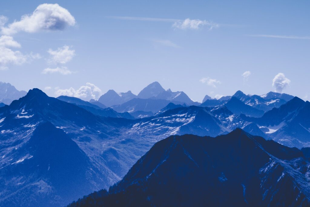 Serene mountain landscape with rugged peaks under vibrant blue sky and wispy white clouds Wallpaper