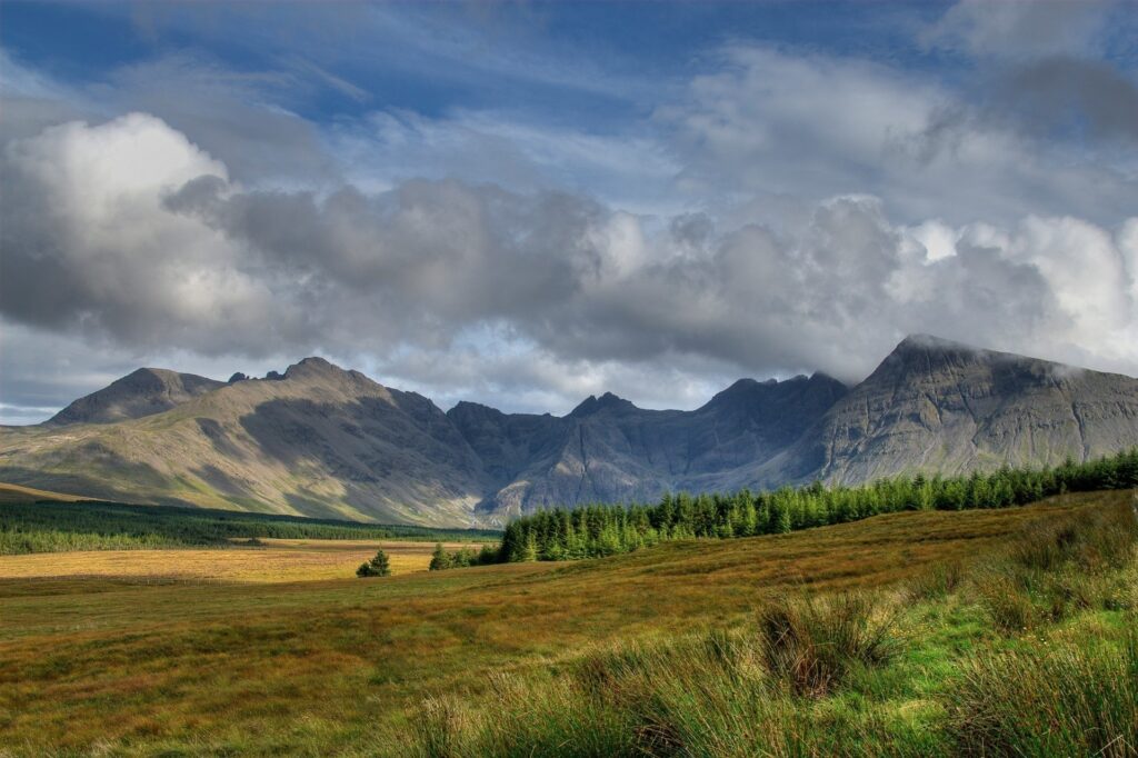 Serene mountain landscape with rugged peaks lush green trees and dramatic cloudy sky wallpaper background