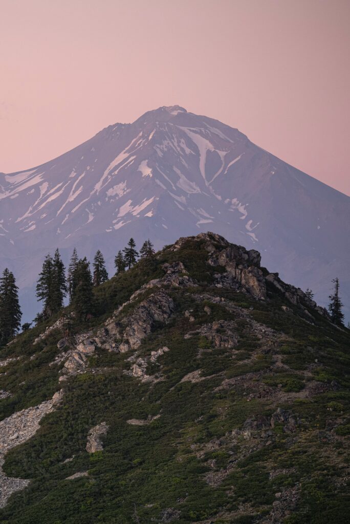 Stunning mountain wallpaper with rocky peak lush green trees and snow-capped summit in pink clouds