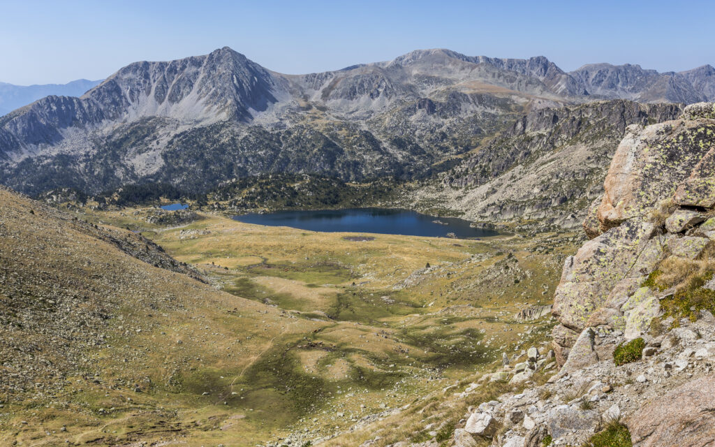 Breathtaking mountain landscape with rugged peaks and tranquil lake in sunlit valley wallpaper background