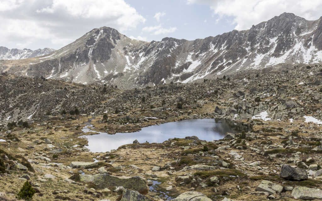 Serene mountain landscape with rugged stones snow patches and lake reflecting clear sky wallpaper