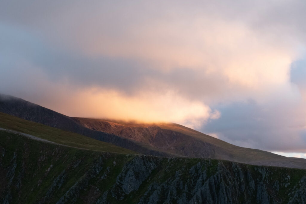 Serene mountain landscape with soft sunlight breaking through clouds illuminating rugged peaks Wallpaper