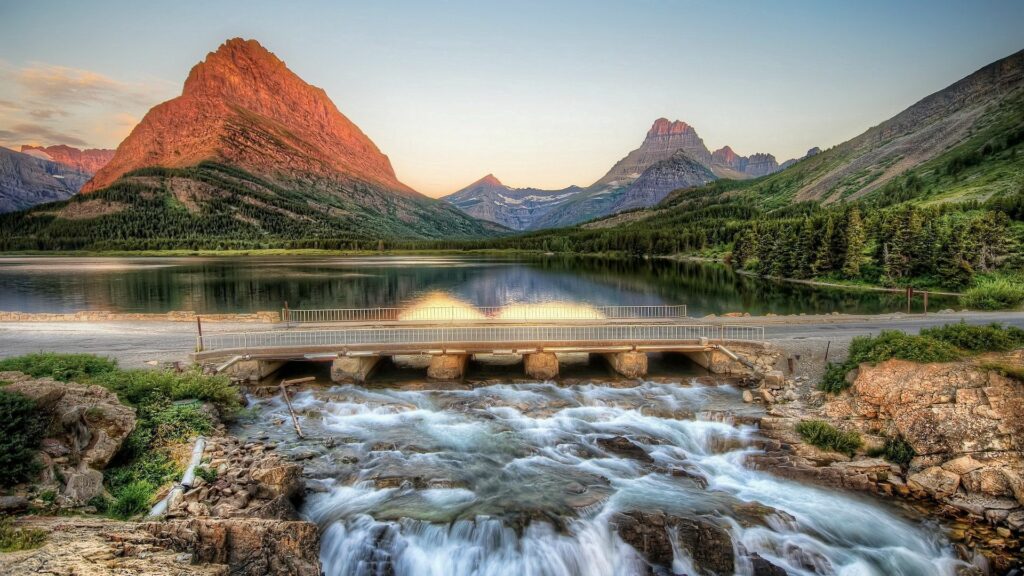 Serene mountain landscape with stone bridge over river lush forests rocky peaks sunrise wallpaper
