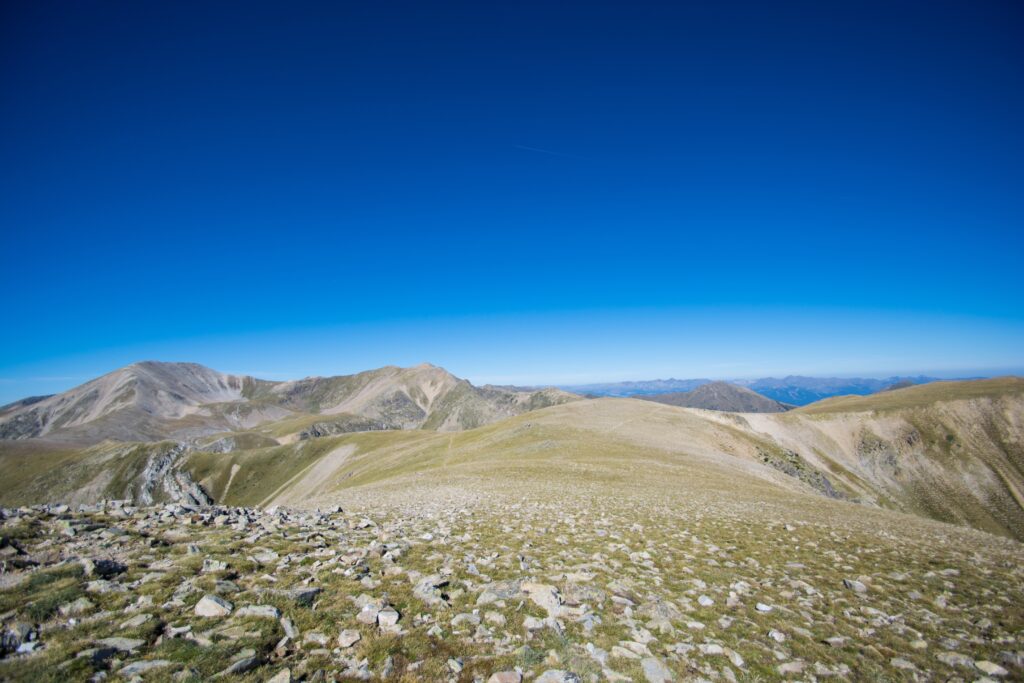 Vast mountain landscape with rocky slopes under deep blue sky creating serene wilderness background Wallpaper