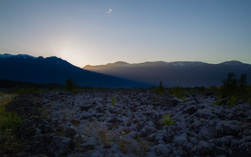 Serene mountain landscape at dusk with golden sun rays and cool blue hues over rocky peaks Wallpaper