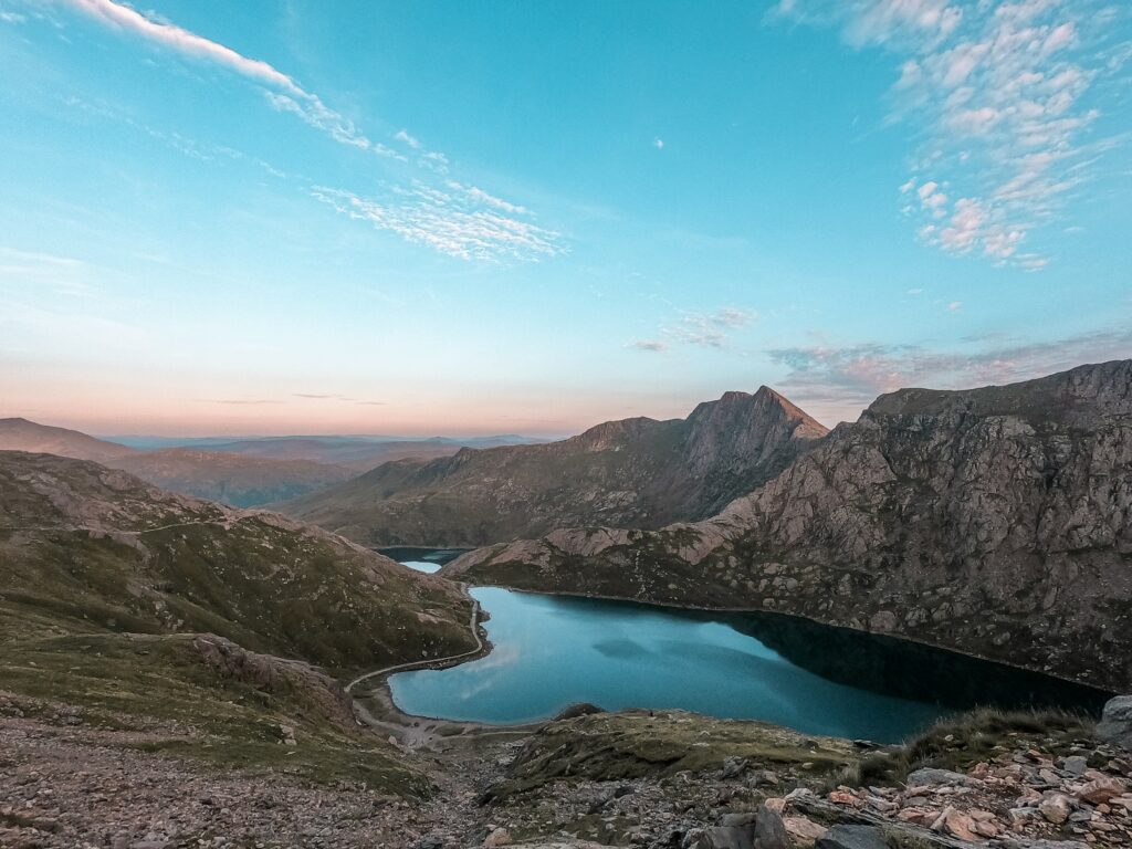 Serene mountain peaks reflected in tranquil blue lake surrounded by rocky hills and greenery Wallpaper