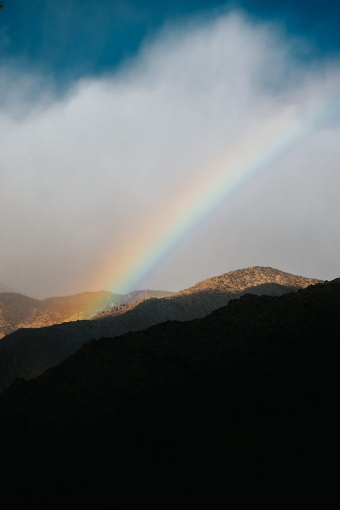 Serene mountain landscape with vibrant rainbow arching over misty clouds against dark peaks Wallpaper