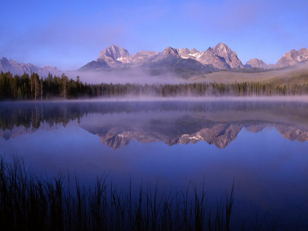 Serene mountain landscape with morning fog over lake reflecting peaks and pine trees wallpaper