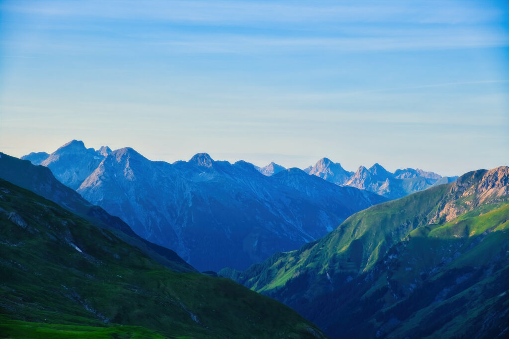 Serene mountain range with lush green slopes and blue ridges in soft daylight wallpaper background