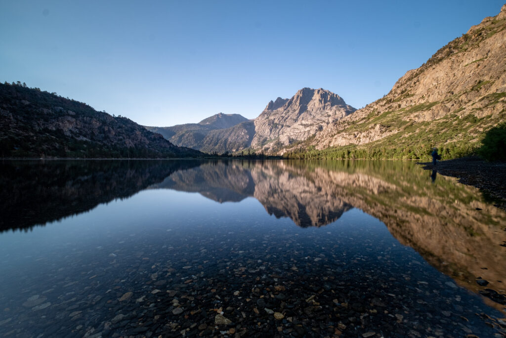 Serene lake reflecting rugged rocks and towering mountains in calm clear water natural landscape Wallpaper