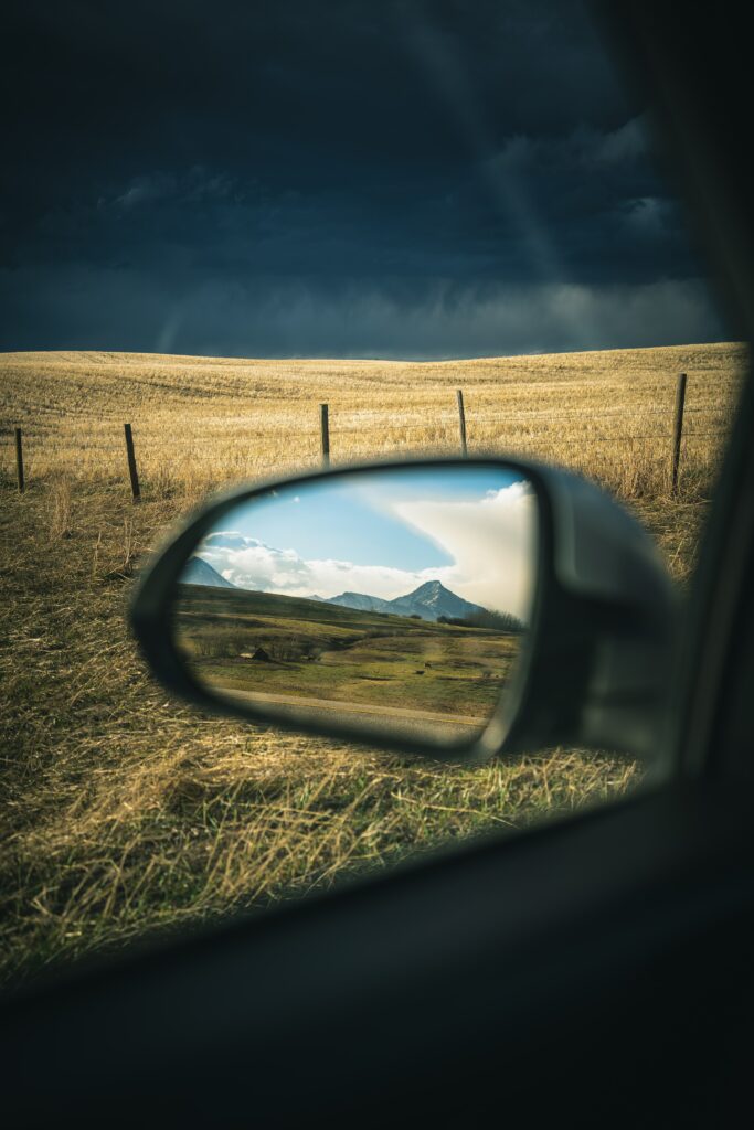 Car side mirror view of mountains golden fields and dramatic dark clouds reflecting nature landscape Wallpaper