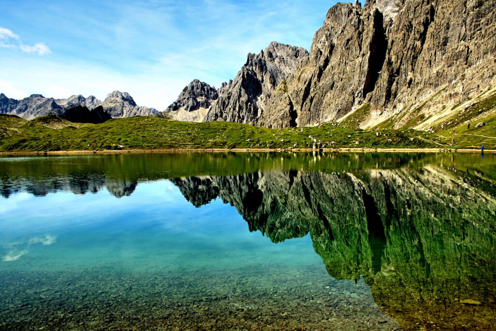 Rugged mountains and rocky cliffs reflected on crystal-clear lake with vivid green and blue hues Wallpaper
