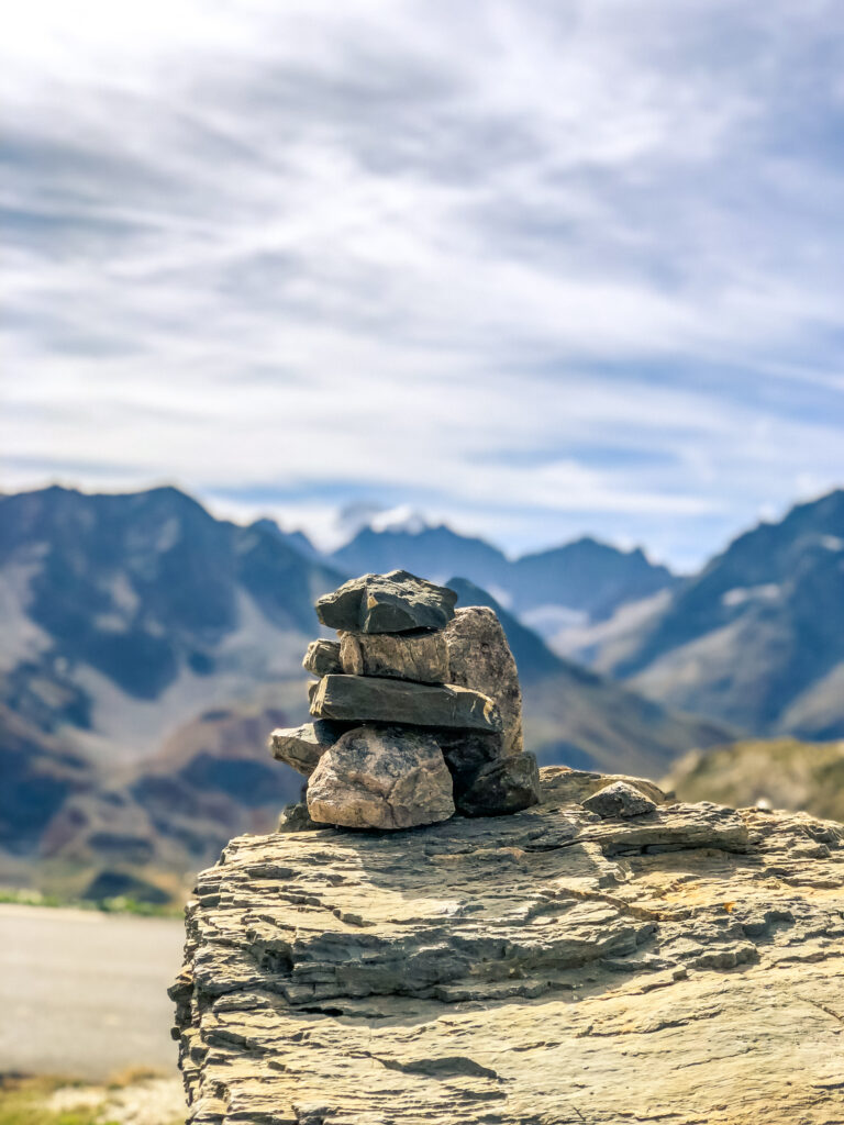 Balanced stone stack on rocky ledge with majestic mountains and cloudy sky background wallpaper