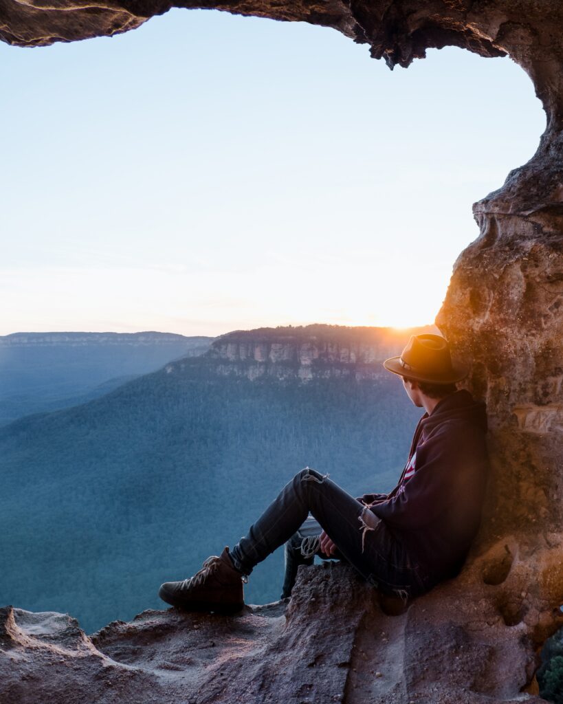 Traveler in rock alcove watching sunset over mountain range serene nature landscape wallpaper