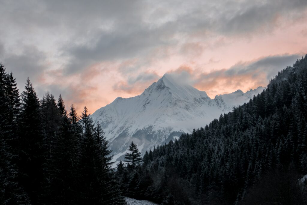 Serene sunset mountain landscape with snow peak dense forest pink orange sky wallpaper background