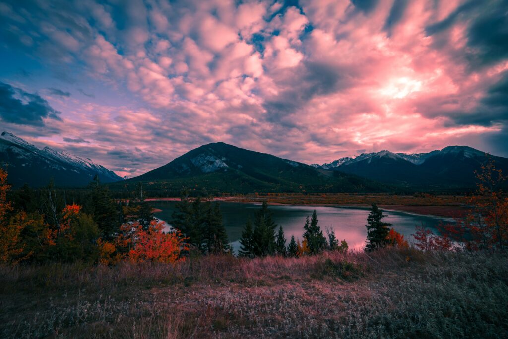 Serene mountain sunset with pink clouds lake reflection autumn trees and snow capped peaks background Wallpaper