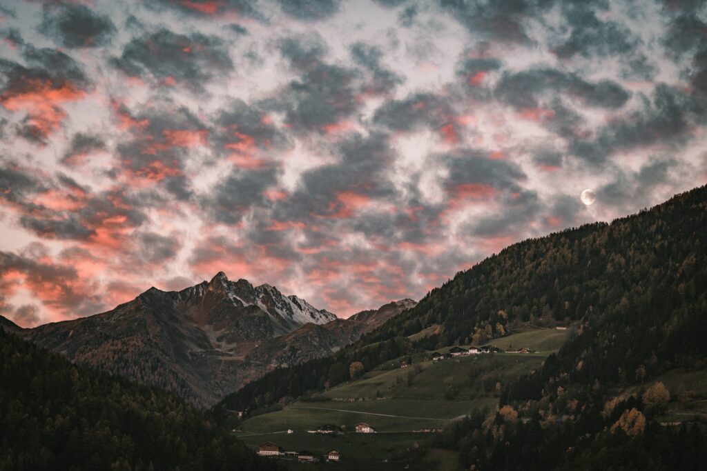 Serene mountain sunset with pink clouds crescent moon village and lush green forest wallpaper background