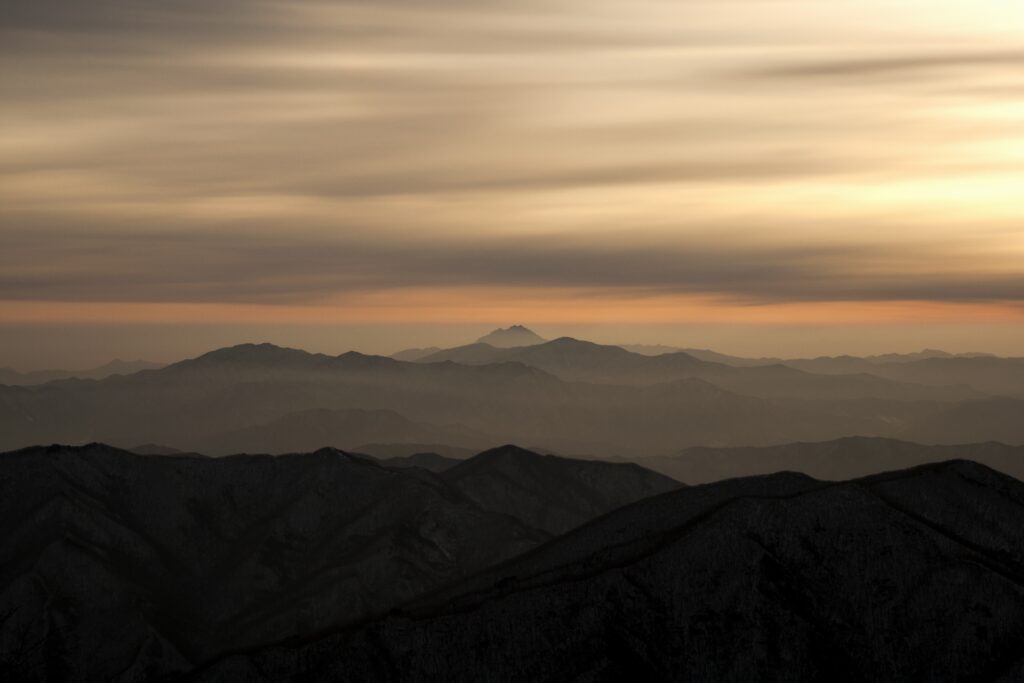 Sunset over foggy mountain ridges with warm orange and gold sky in serene landscape wallpaper