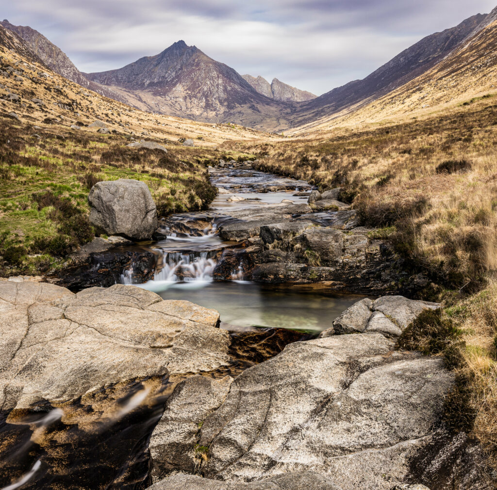 Serene mountain landscape with clear stream over stones in valley under cloudy sky wallpaper background