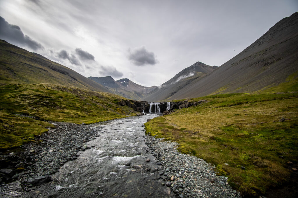 Serene mountain valley with clear stream colorful pebbles grassy banks and cloudy sky wallpaper
