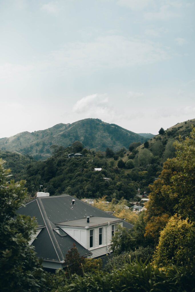 Aerial view of a peaceful house surrounded by lush trees and mountains under cloudy sky wallpaper