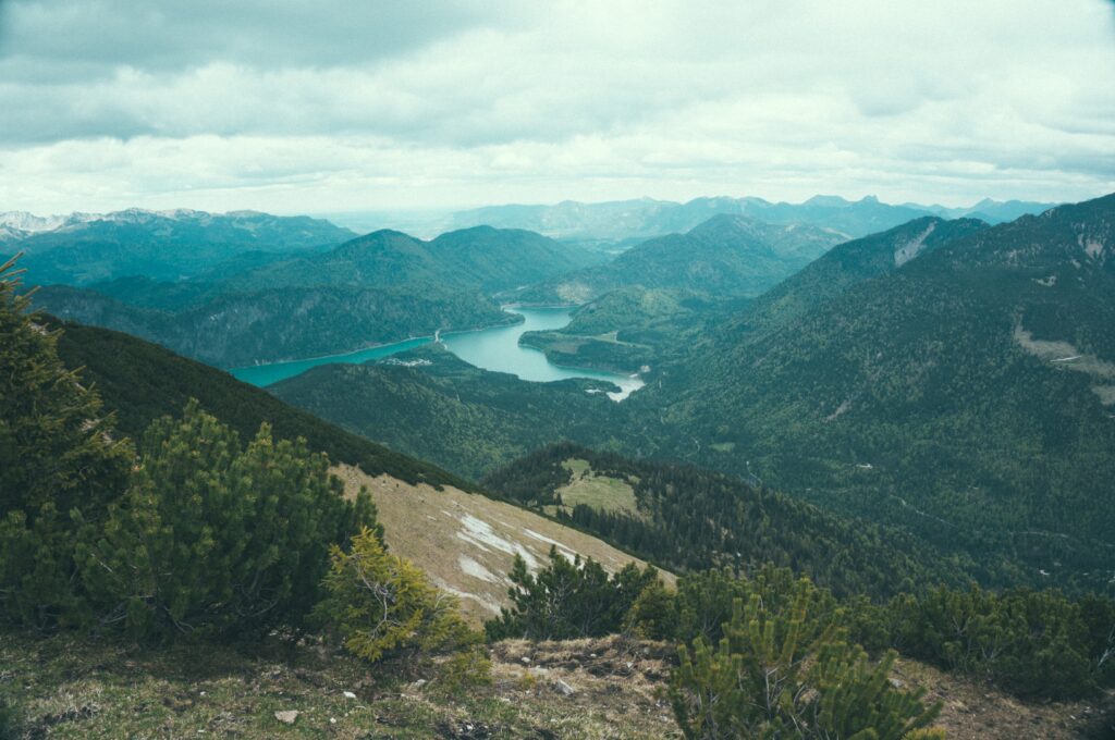 Aerial view of serene mountains winding lake lush green forests under cloudy sky wallpaper background