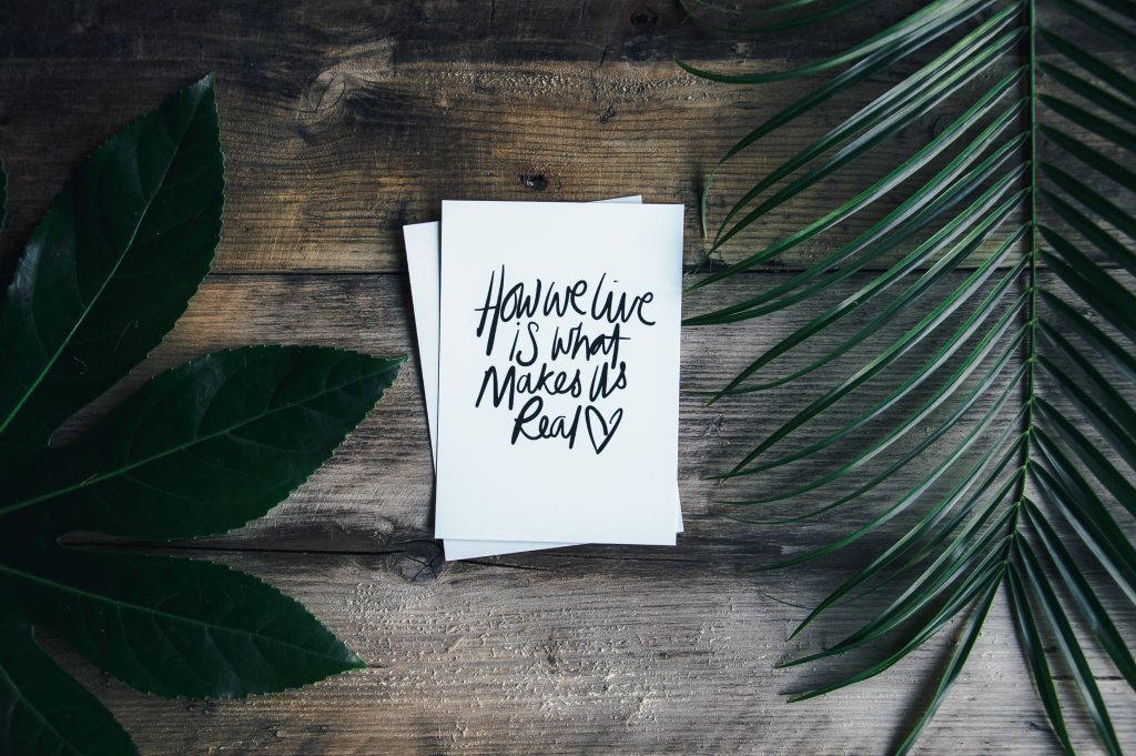 Handwritten quote on white card with tropical leaves and dark wood rustic background wallpaper