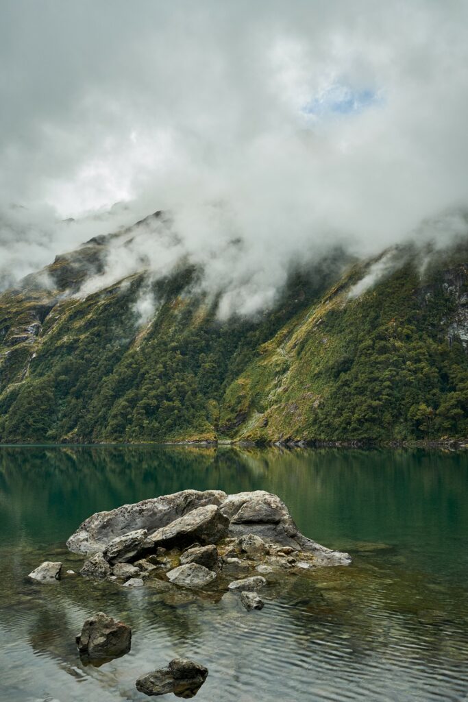 Serene New Zealand lake reflecting misty mountains rugged rocks and lush green slopes wallpaper