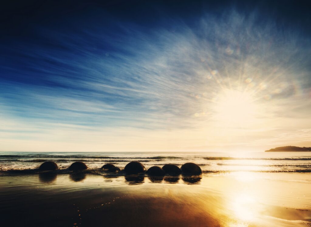 Serene New Zealand sunrise over ocean with spherical rocks and reflective shoreline wallpaper background