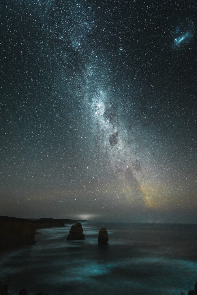 Serene night beach wallpaper with Milky Way stars shimmering over calm ocean and rocks