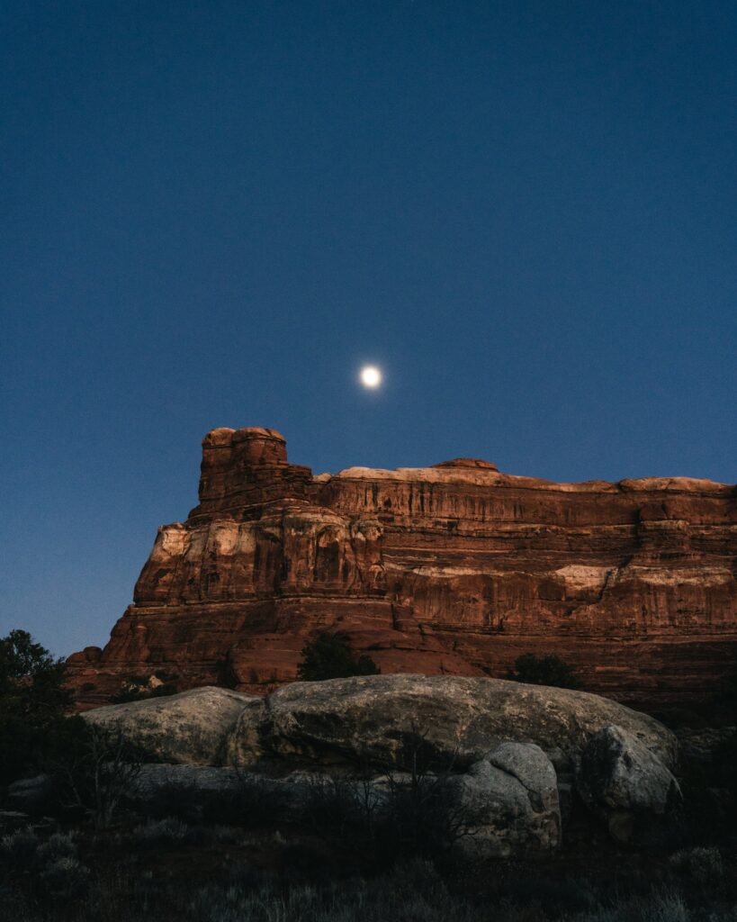 Serene night canyon landscape with full moon glowing over rugged sandstone rocks wallpaper background