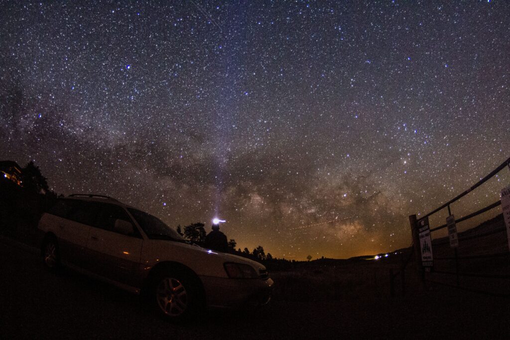 Car parked under vast starry sky with Milky Way glowing serene night adventure wallpaper background