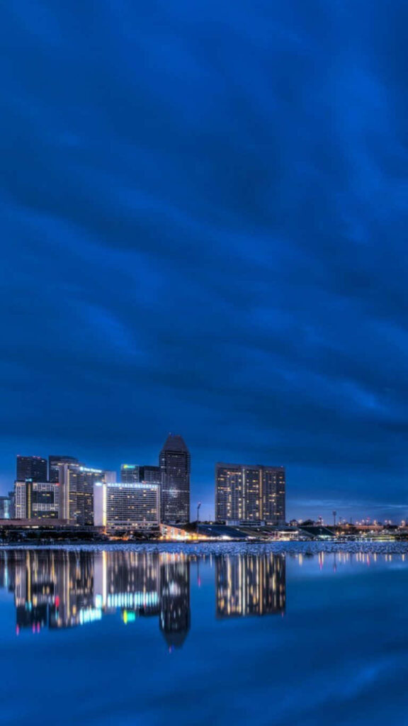 Tranquil Night Cityscape Wallpaper with Reflective Water & Blue Sky