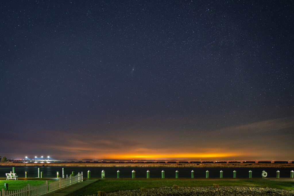 Serene night landscape with calm river promenade under starry sky and distant city lights wallpaper