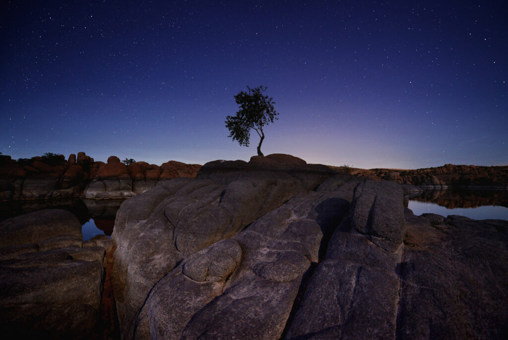 Serene night landscape with rugged stone blocks weathered wood and solitary tree under stars Wallpaper