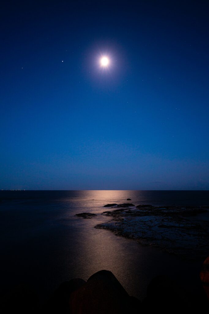 Serene night wallpaper with bright moon and stars reflecting on calm sea with clouds and rocks