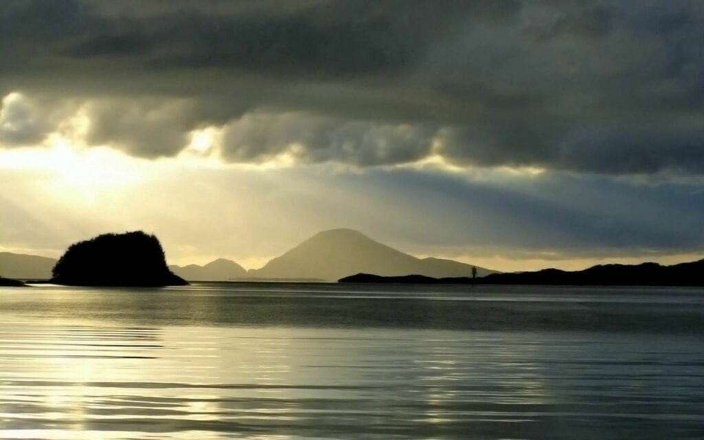 Serene night sea with gentle ripples silhouetted mountains islands and dramatic light rays background Wallpaper