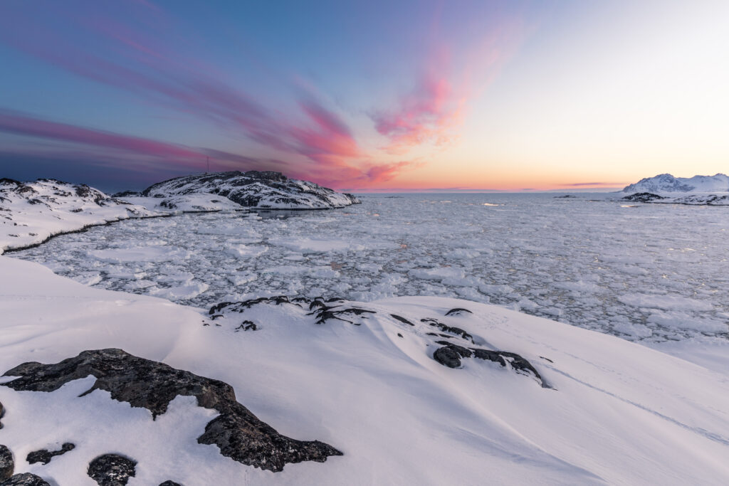 Snowy northern coast with icy rocks and frozen ocean under pastel pink and purple arctic sky Wallpaper