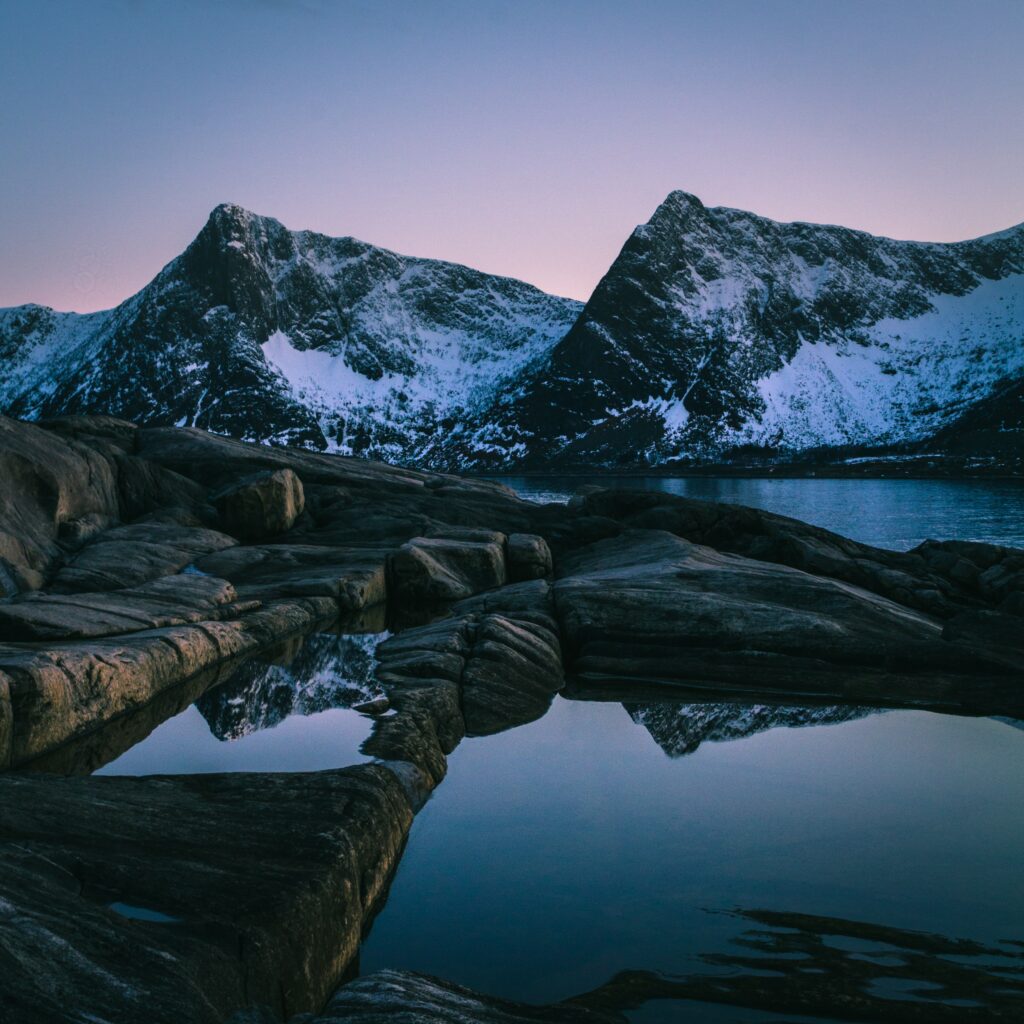 Serene sunset over snowy Norwegian mountains reflected in calm lake with dusky blue purple sky Wallpaper