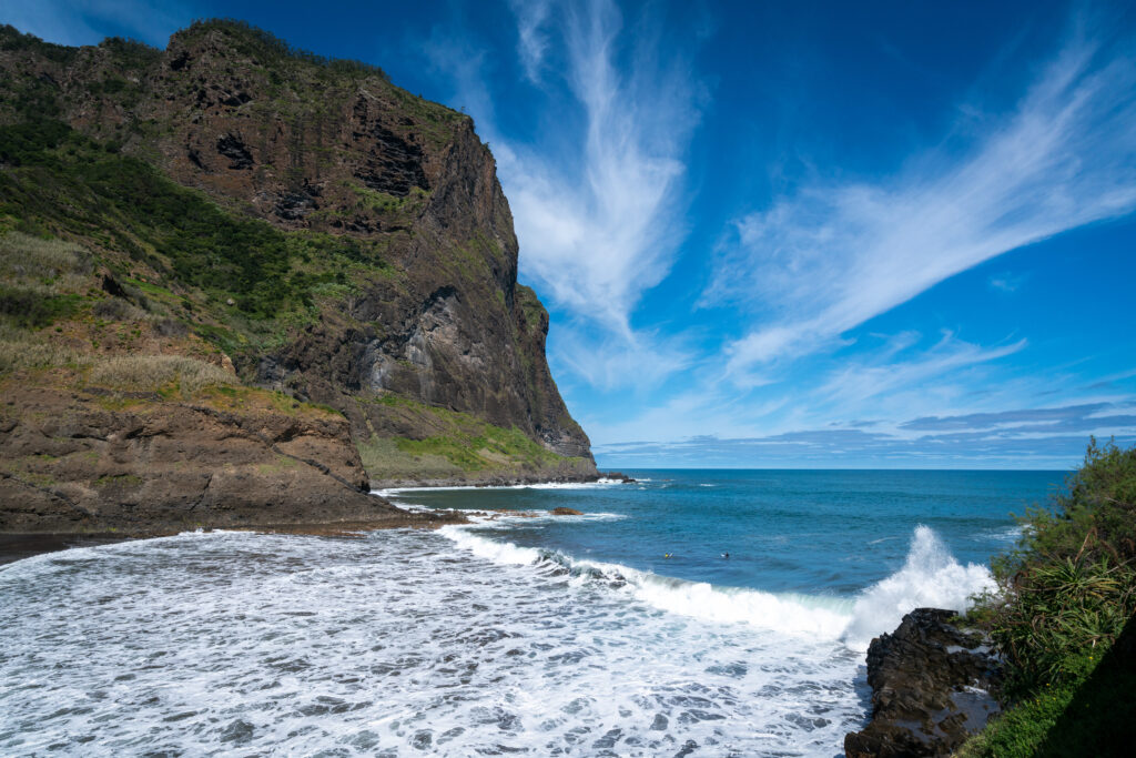 Serene ocean bay with rugged rocks cliffs and vibrant blue waves under bright cloudy sky wallpaper