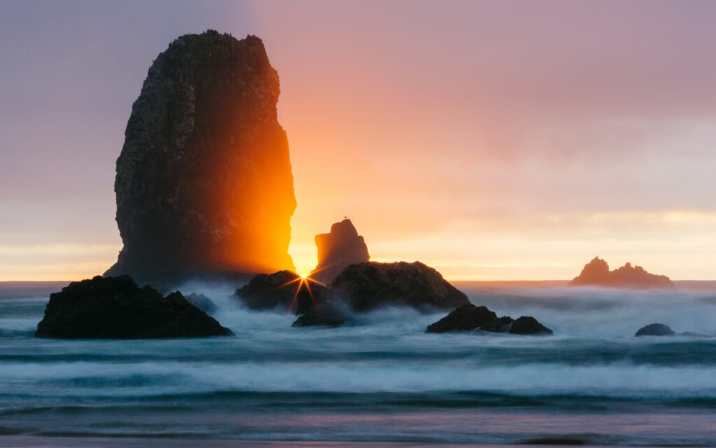 Serene ocean wallpaper with golden sunset light on dramatic rocks and misty blue surf background