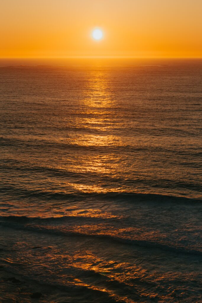Serene ocean sunset wallpaper with gentle waves and warm orange glow reflecting on water