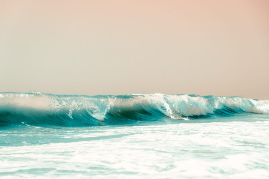 Serene ocean wave rolling over crystal blue water under soft peach sky natural wallpaper background