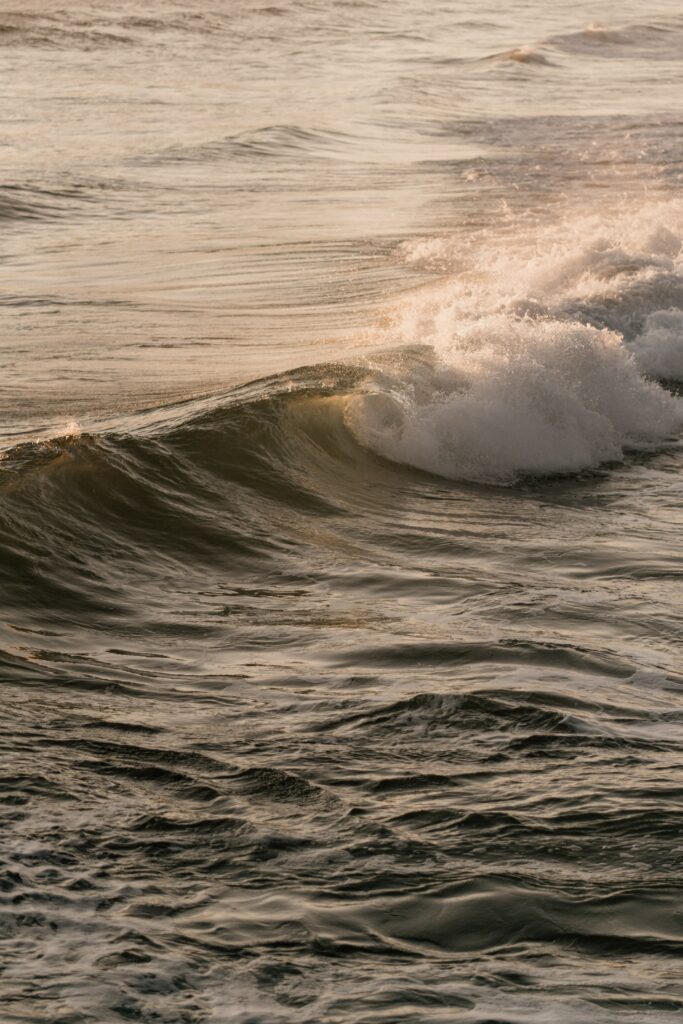 Ocean wave with sunlight glinting on water and white spray cresting calm serene wallpaper background